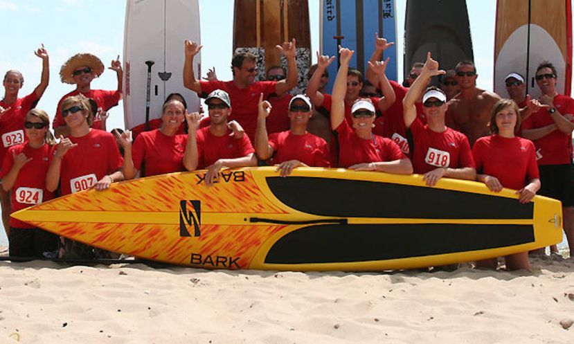 Participants in a race held by Surftech pose behind one of Surftech&#039;s many high-performing stand up paddle boards. Photo Credit: A Day At the Beach