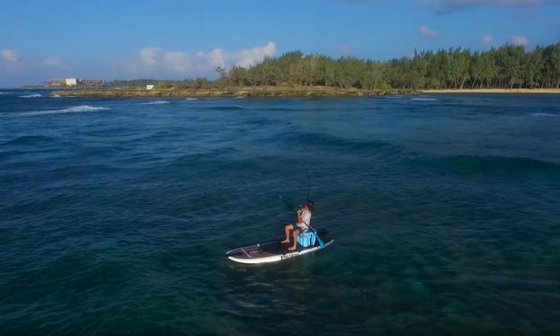 Todd Caranto reels in a fish after hooking it while SUP surfing a wave. 